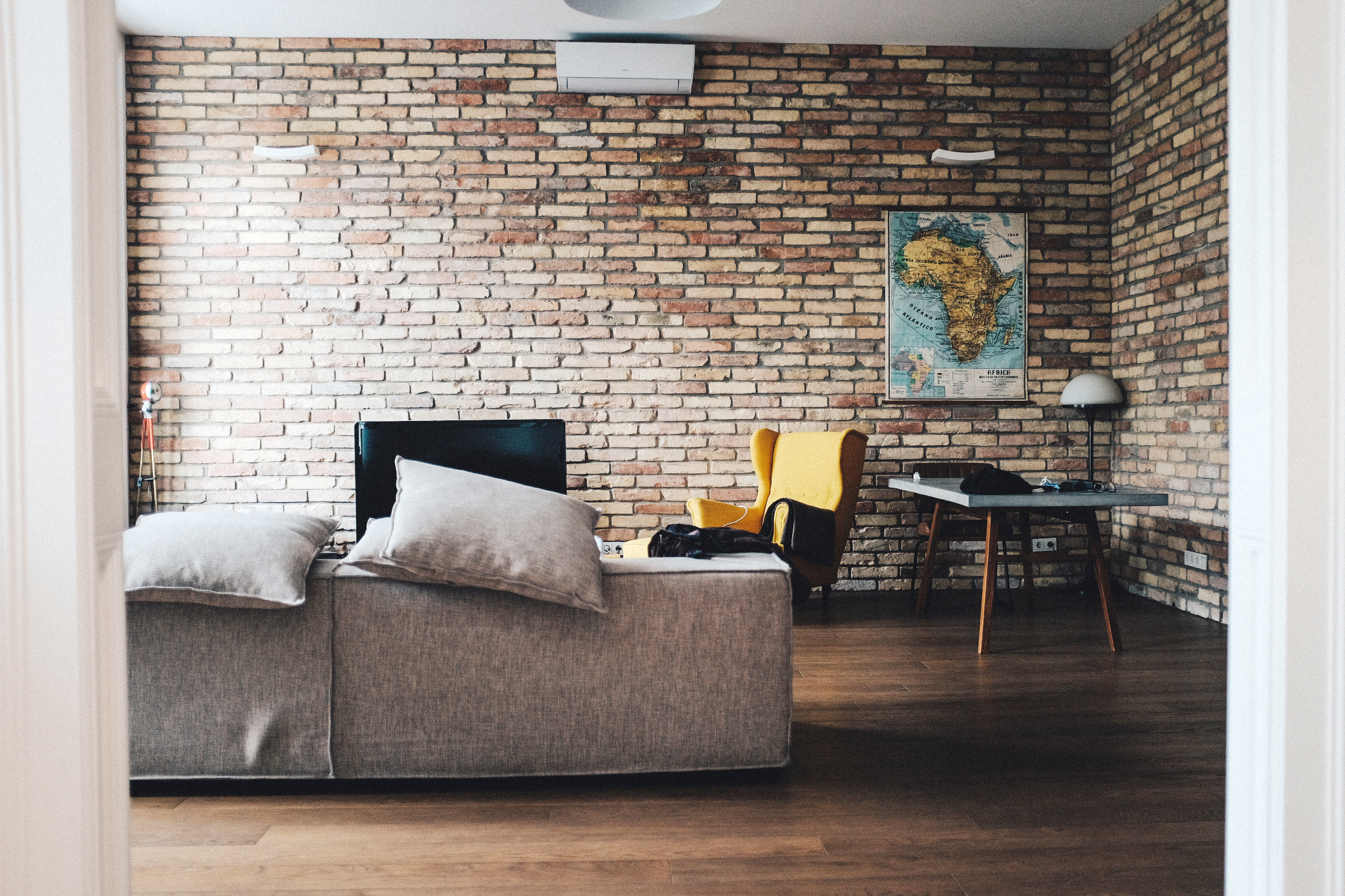  Wall to Wall Exposed Brick Living Room with Couch, Yellow Chair, Modern Table, Map of Africa on the Wall