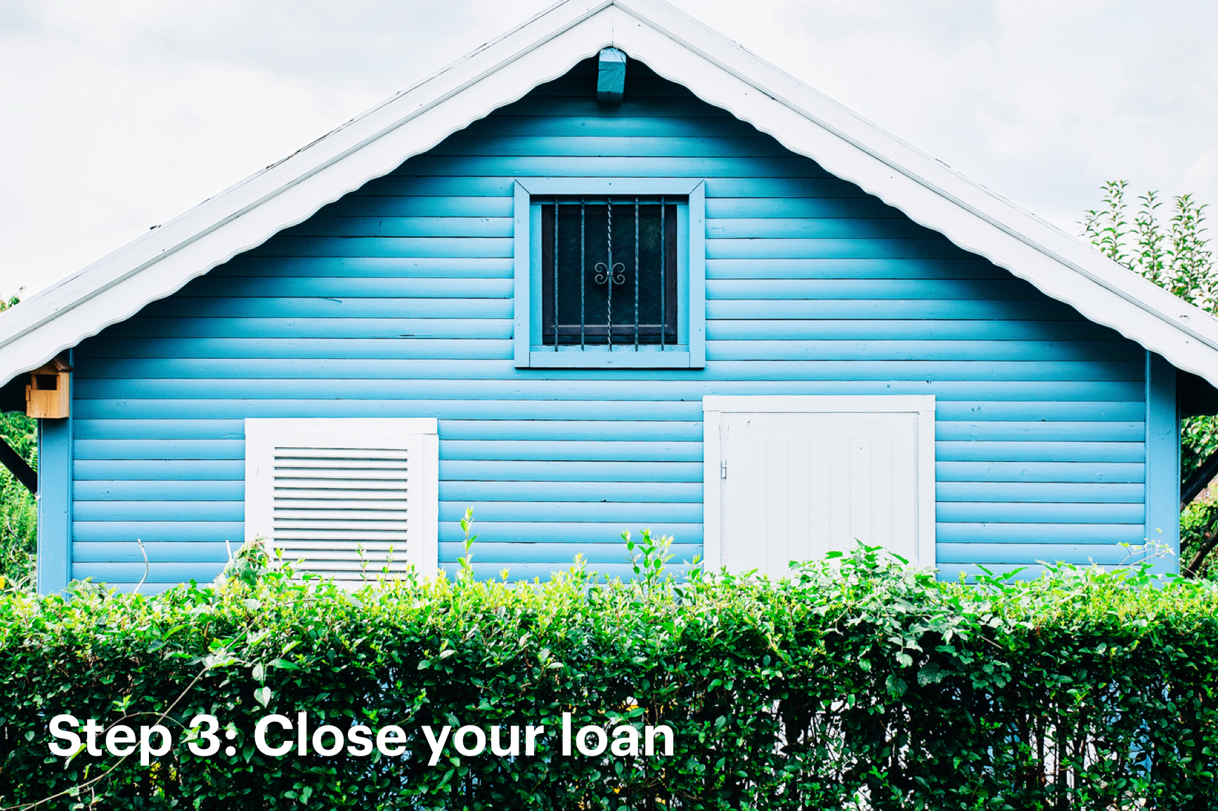  Close Up of Side Panel of Blue Home Behind Green Shrubs with Text that Reads: Step 3: Close Your Loan
